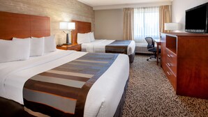 A hotel room with two beds, a desk, a television, and a patterned carpet.