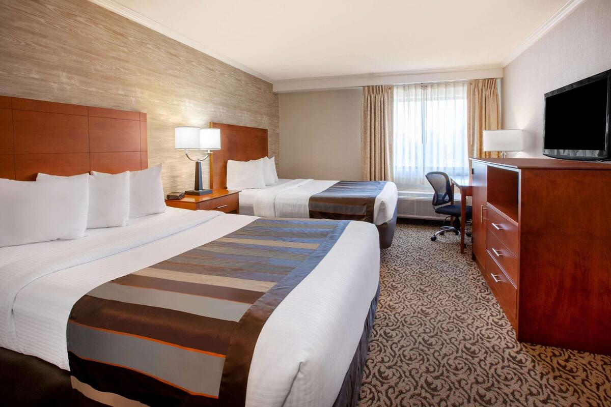 A hotel room with two beds, a desk, a television, and a patterned carpet.