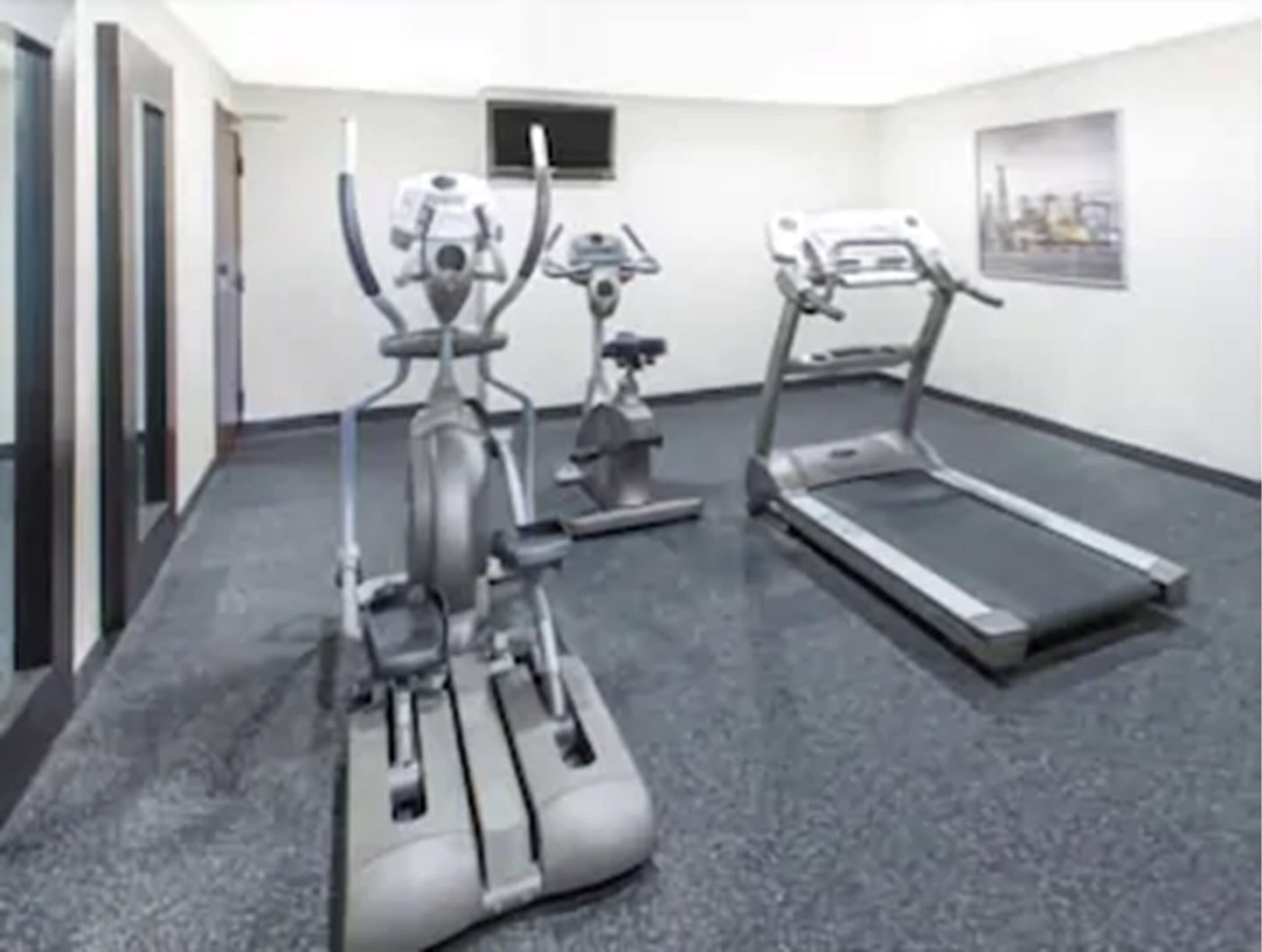 A fitness room with cardio equipment including a treadmill and elliptical machines.