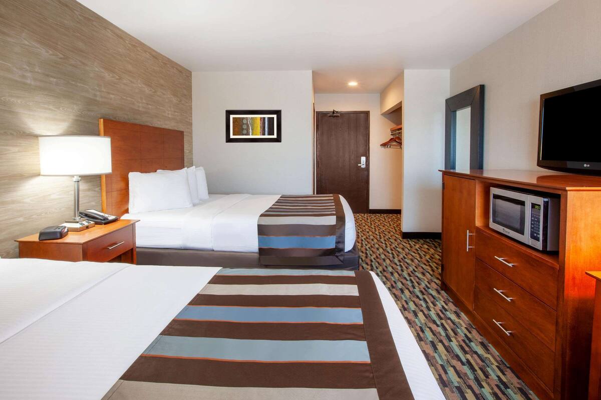 A hotel room with two beds, a desk with a lamp, a television, a microwave, and a wardrobe.