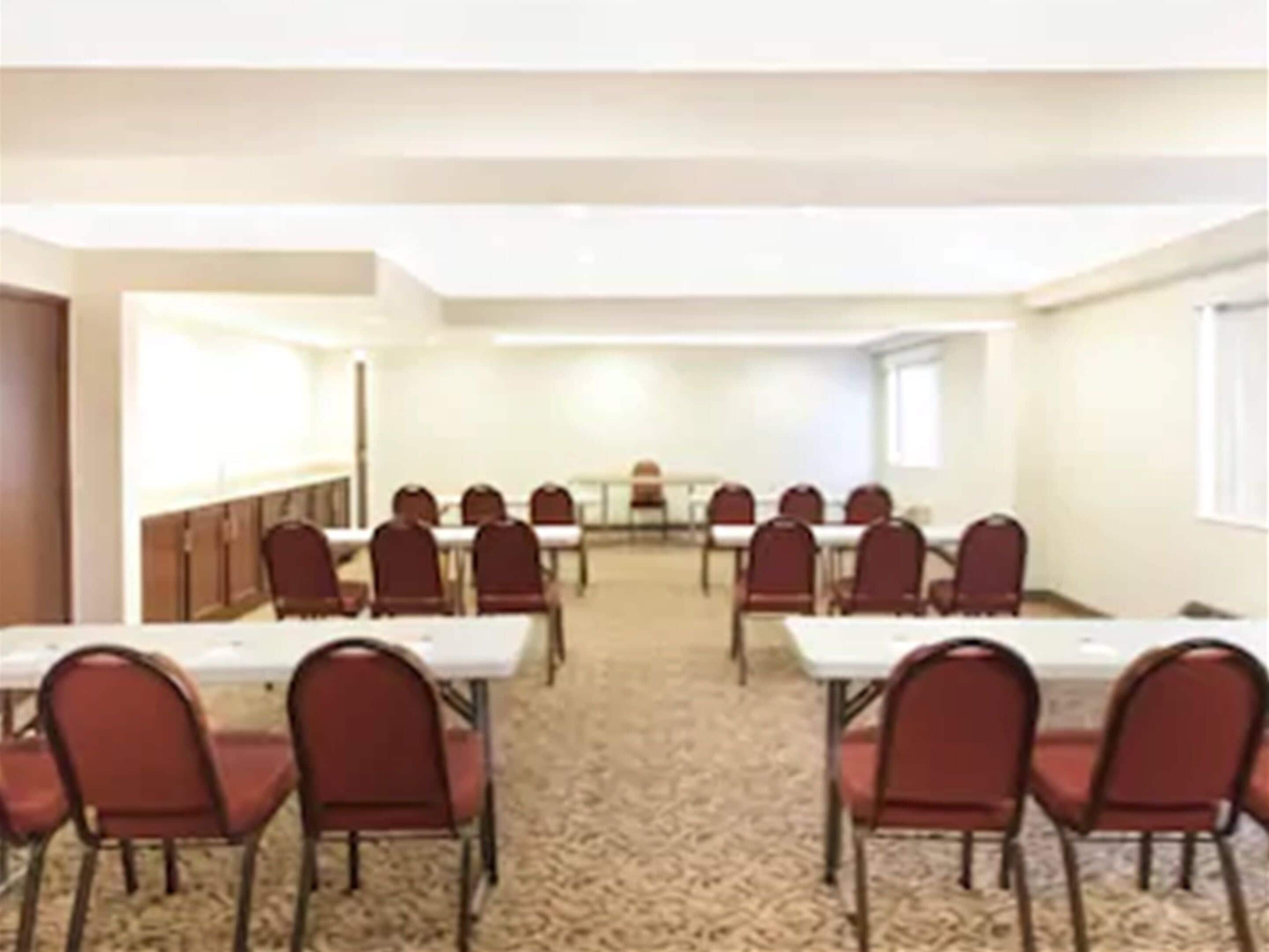 A conference room with rows of tables and chairs, carpeted floor, and white walls.