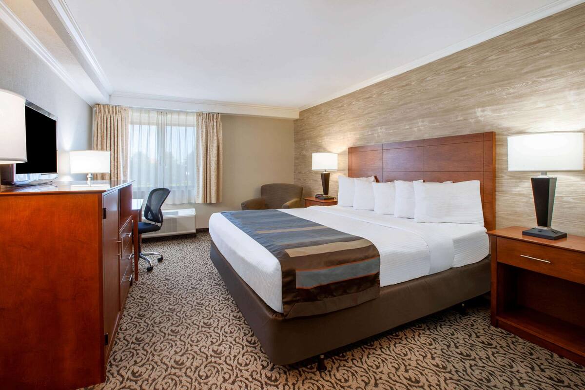 A hotel room with a large bed, a desk with a chair, a TV, and a lamp.