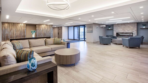 A spacious hotel lobby with a modern design, featuring a large sofa, a round coffee table, and a seating area with armchairs.