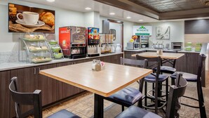 A modern breakfast area with a coffee machine, a pastry display, and a seating area with tables and chairs.