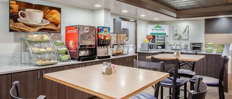A modern breakfast area with a coffee machine, a pastry display, and a seating area with tables and chairs.