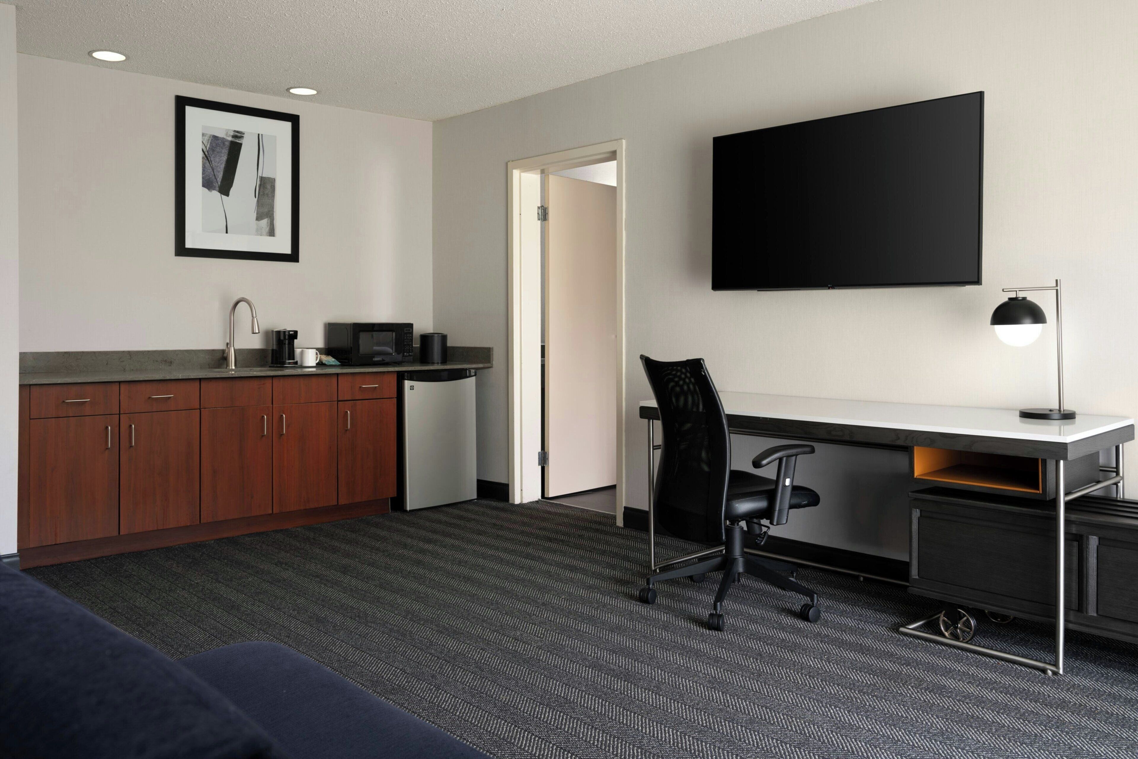Habitación de hotel con kitchenette, televisión de pantalla plana, escritorio con silla y sofá.