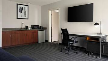 Habitación de hotel con kitchenette, televisión de pantalla plana, escritorio con silla y sofá.