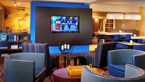 A hotel lobby with seating, a TV displaying a motorcycle race, and a bar area. - Courtyard by Marriott Detroit Utica (Utica)