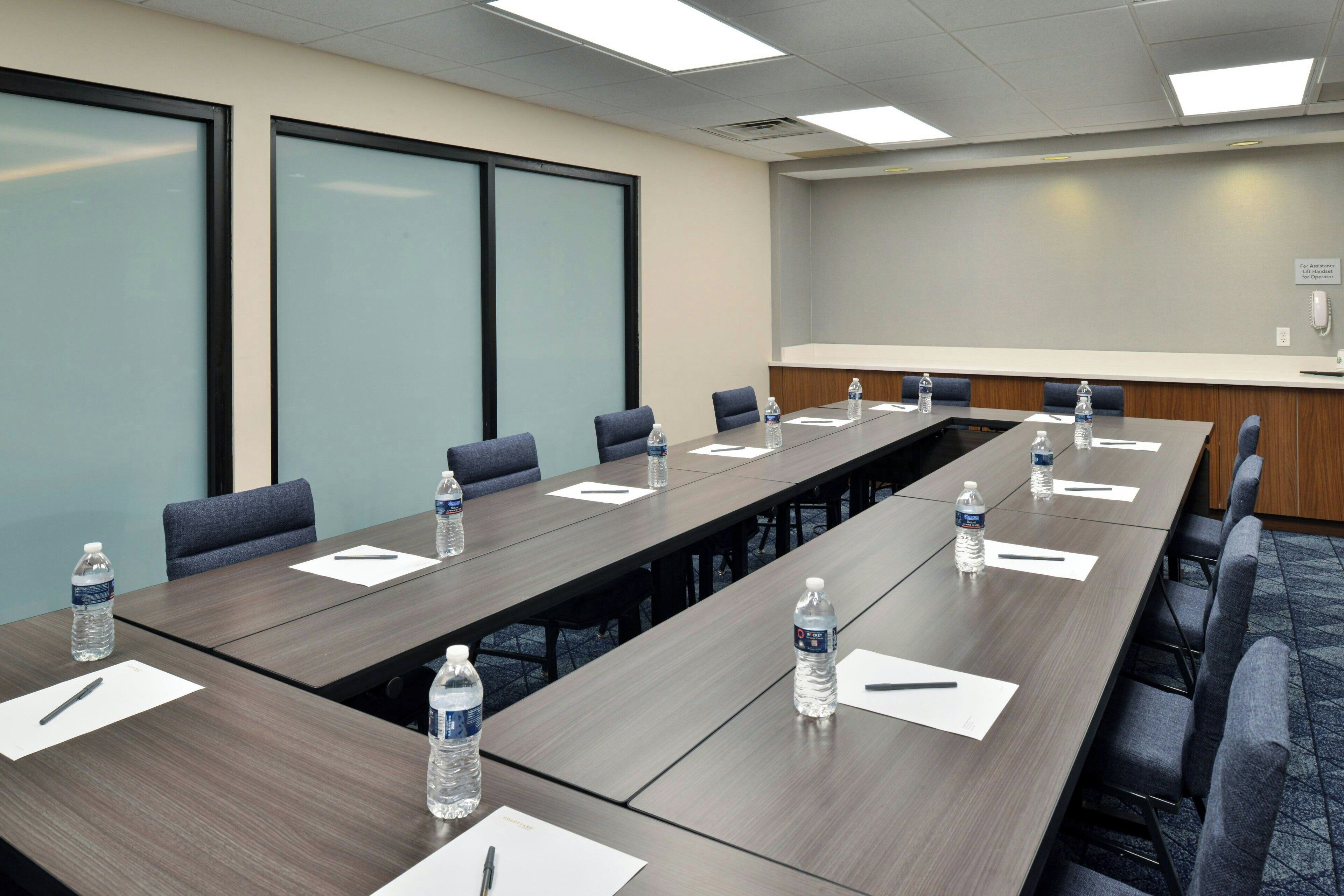 A conference room with a long table, chairs, water bottles, and a projector screen.