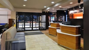 A hotel lobby with a reception desk, seating area, and a view of the street outside. - Courtyard by Marriott Detroit Utica (Utica)