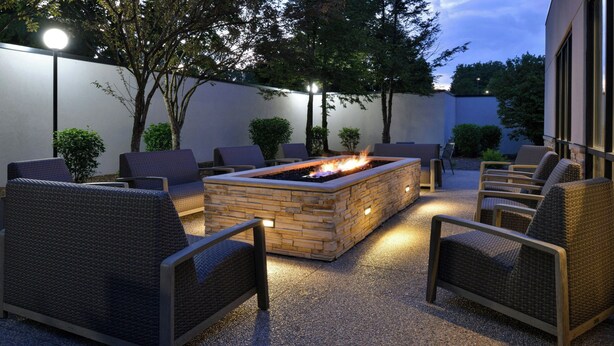 An outdoor seating area with a fire pit, surrounded by wicker chairs and a stone fire table. - Courtyard by Marriott Detroit Utica (Utica)
