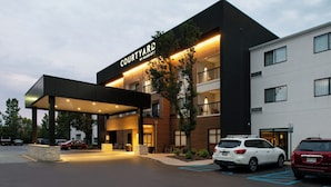 A modern hotel entrance with a covered outdoor area, multiple floors, and a parking lot. - Courtyard by Marriott Detroit Utica (Utica)