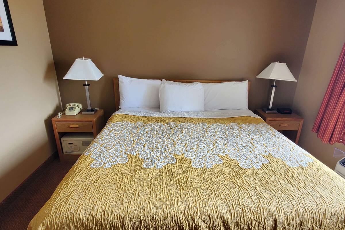 A hotel room with a large bed, two bedside tables, a lamp on each table, and a telephone on one of the tables.