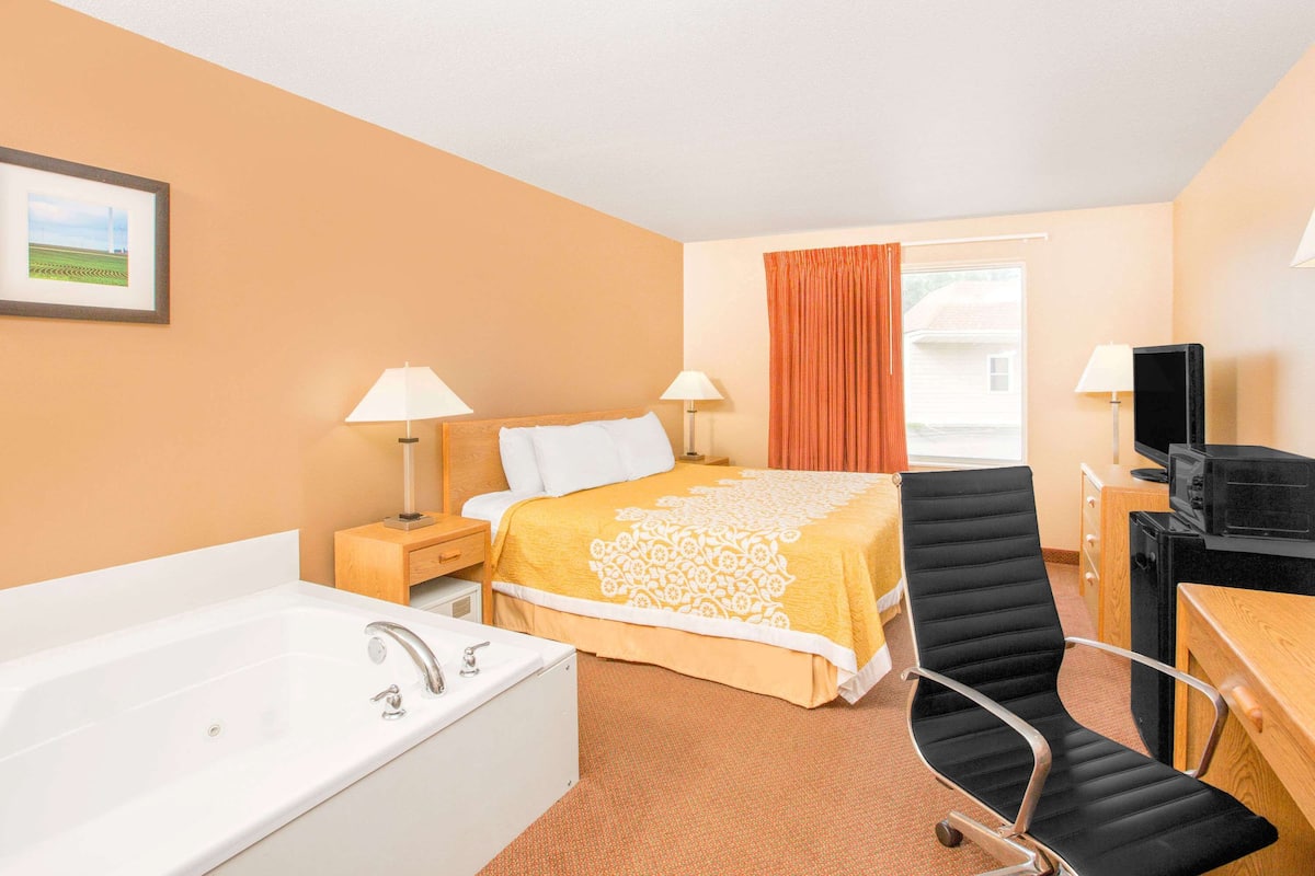 A hotel room with a bed, a desk, a chair, a television, a lamp, a picture on the wall, and a window with curtains.