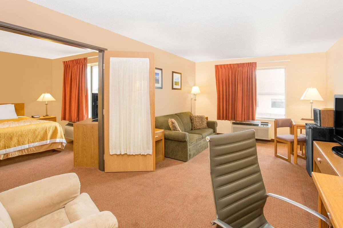 A hotel room with a bed, a sofa, a desk with a computer, a chair, and a television.