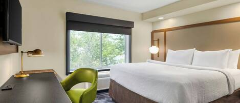 A hotel room with a bed, a desk, a chair, a TV, and a window with a view of trees.