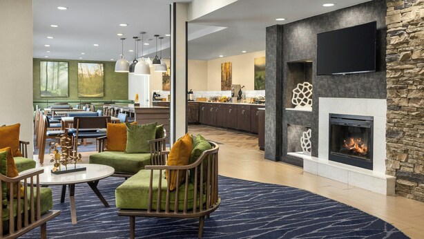 A modern hotel lobby with a fireplace, seating area, and a kitchen in the background. - Fairfield Inn by Marriott Hattiesburg (Hattiesburg)