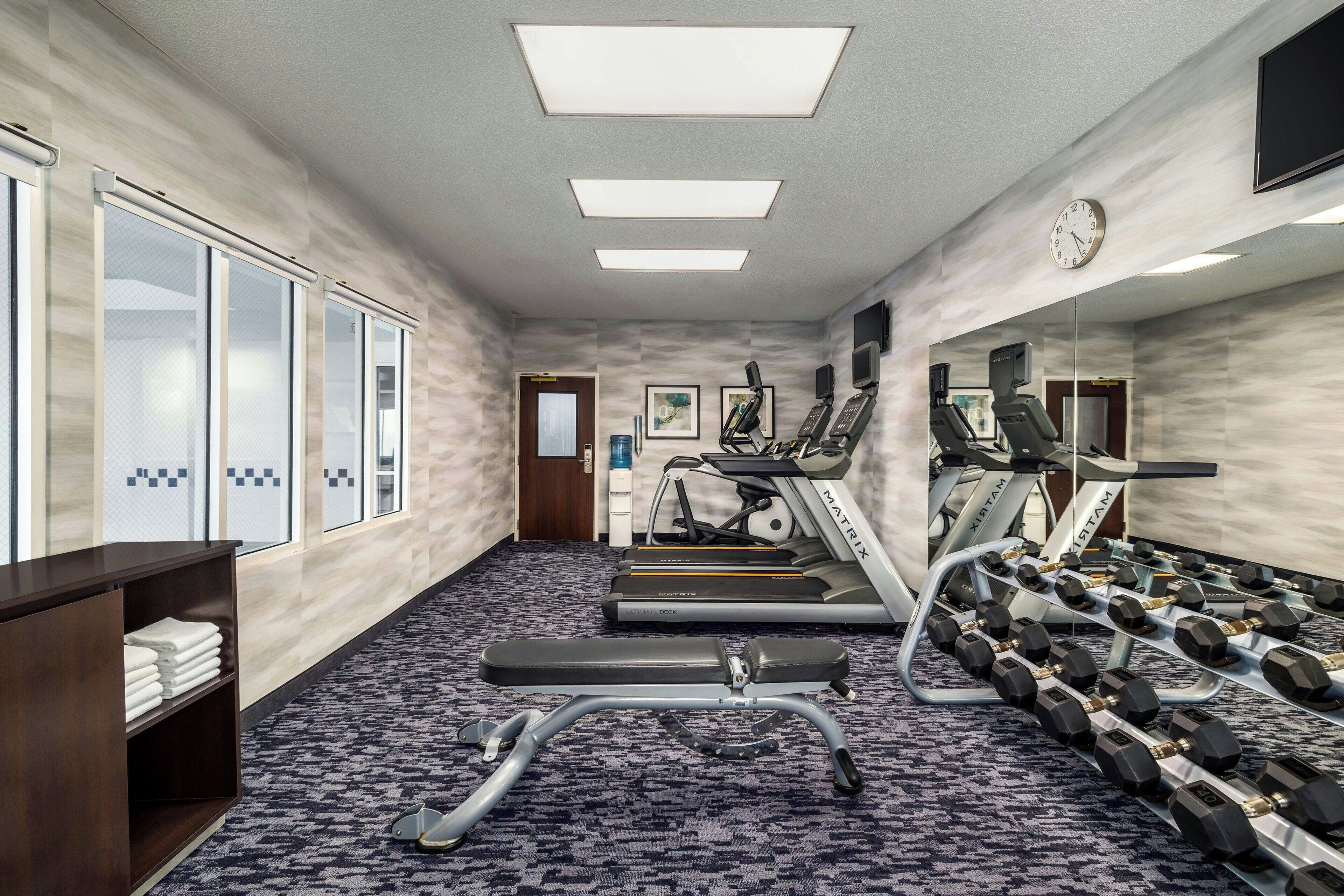 A hotel gym with exercise equipment, a clock, and a large window.