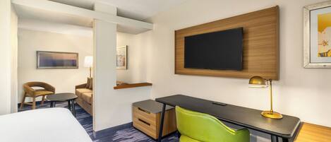 Una habitación de hotel con una cama, un escritorio, una silla verde, un televisor y una lámpara.