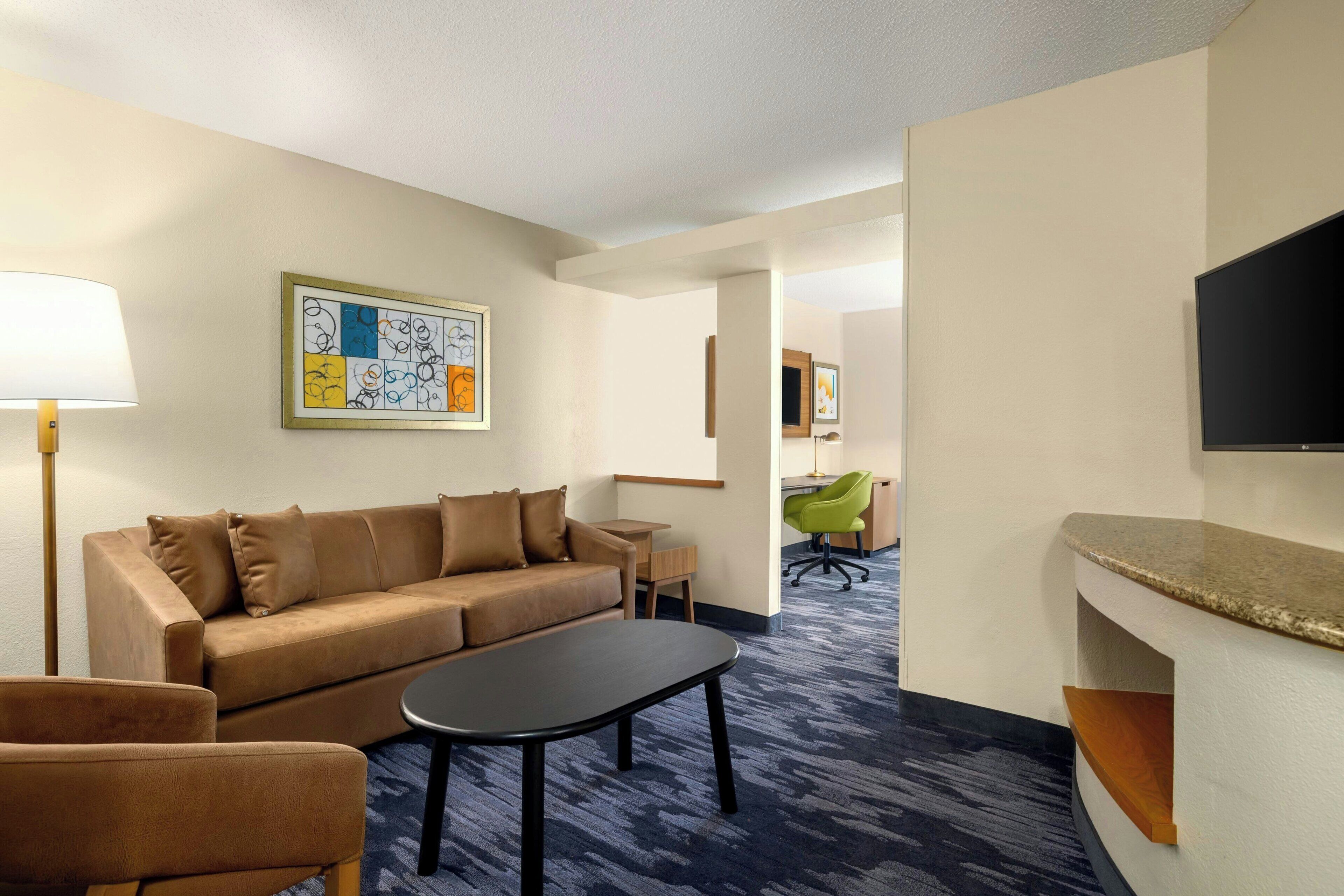 A hotel room with a sofa, a small table, a TV, and a desk with a chair.