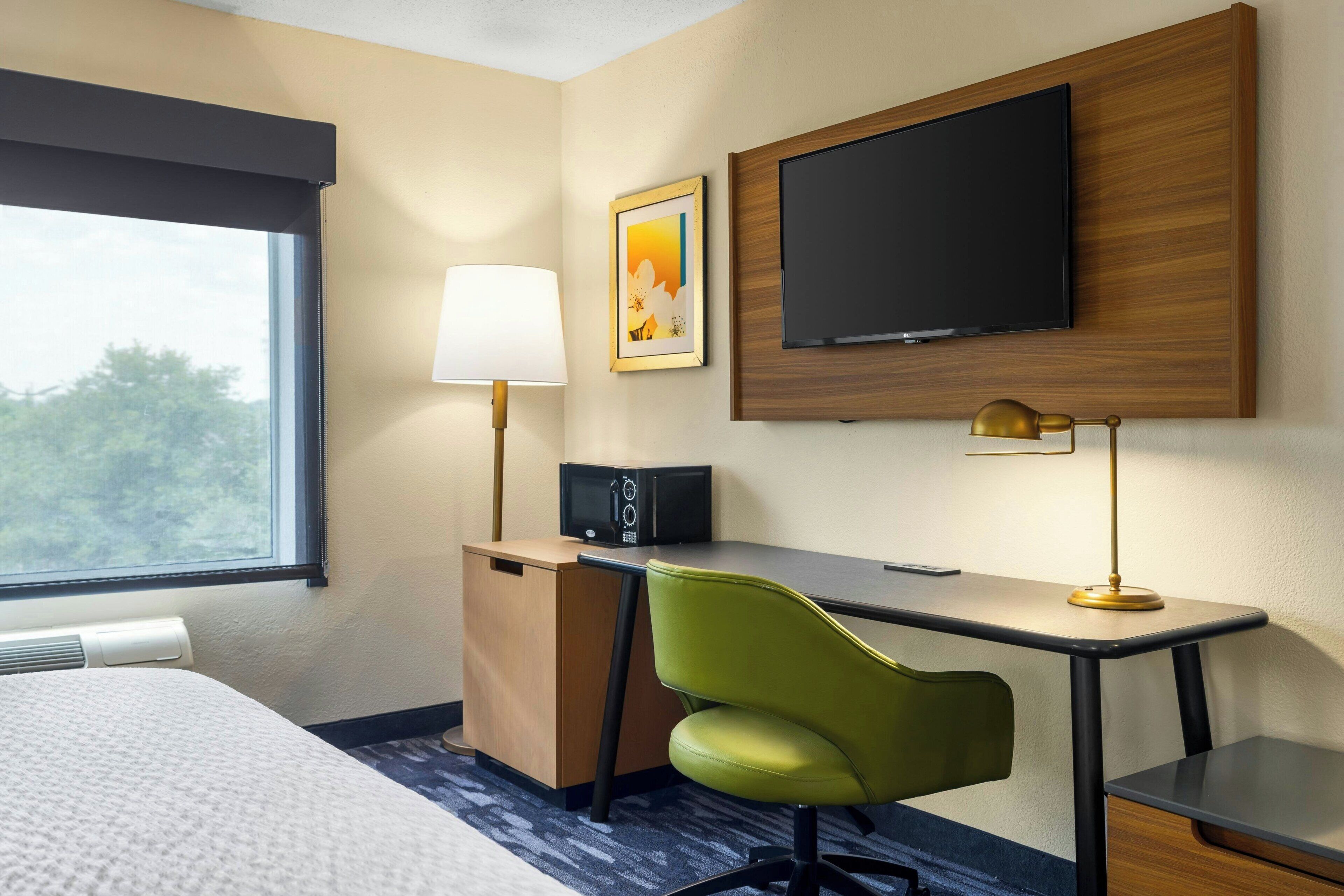 A hotel room with a bed, desk, chair, TV, lamp, and a picture on the wall.
