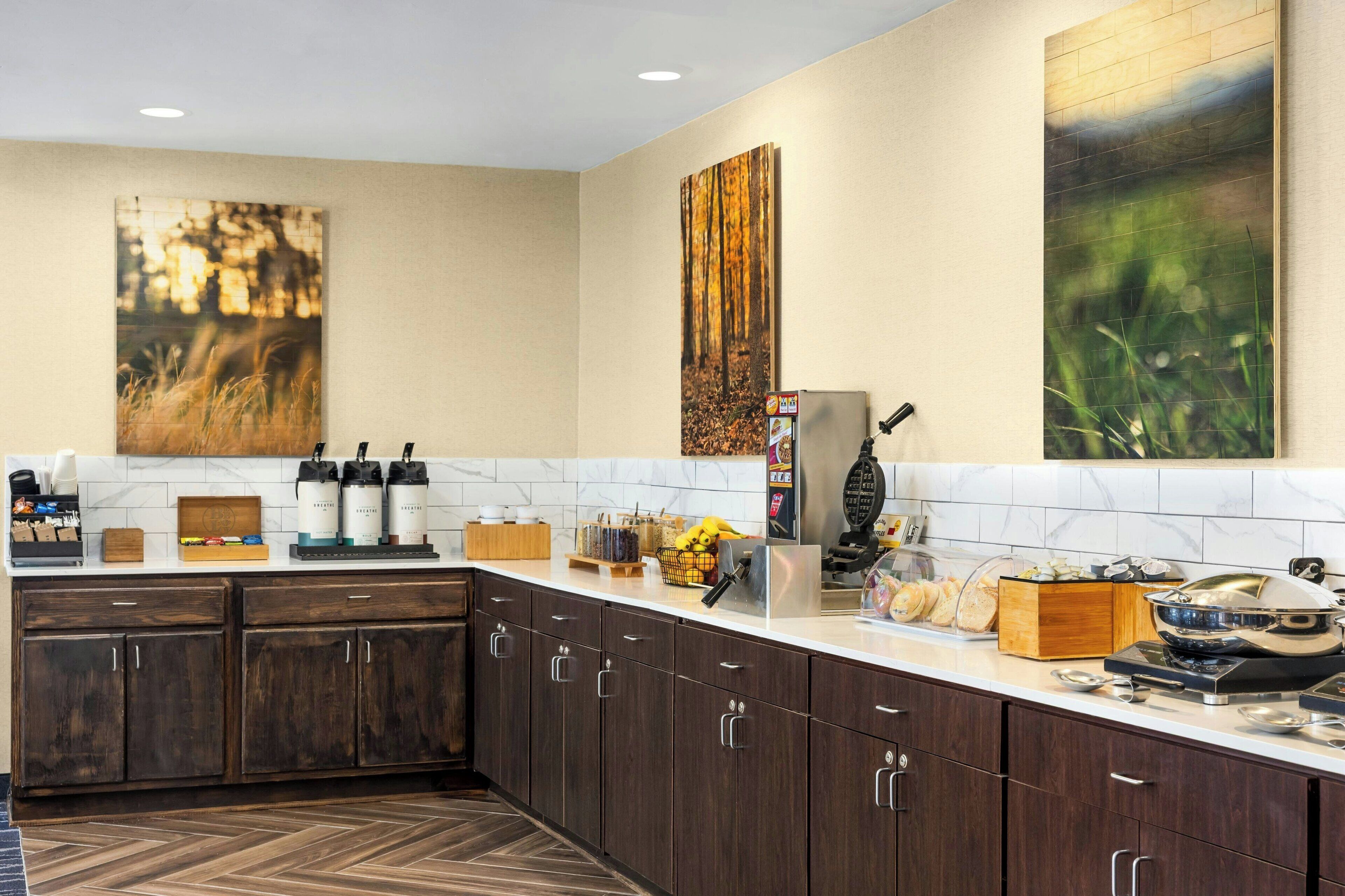 A modern kitchen with dark wood cabinets, white marble backsplash, and artwork on the walls.