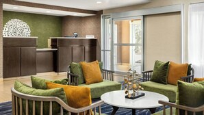 A hotel lobby with a reception desk, seating area with sofas and armchairs, a coffee table, and a decorative plant. - Fairfield Inn by Marriott Hattiesburg (Hattiesburg)