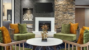 A modern living room with two green sofas, a round coffee table, and a fireplace. - Fairfield Inn by Marriott Hattiesburg (Hattiesburg)