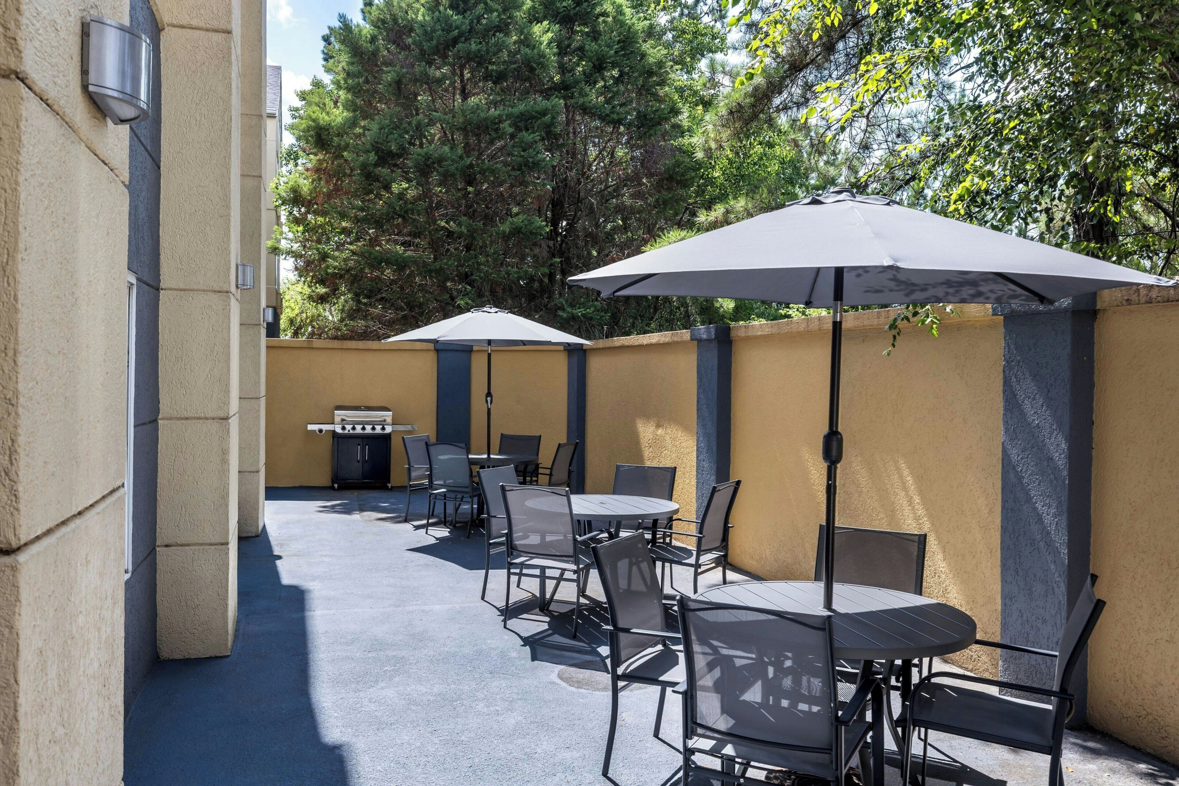Un patio al aire libre con mesas, sillas, una parrilla y sombrillas que dan sombra.