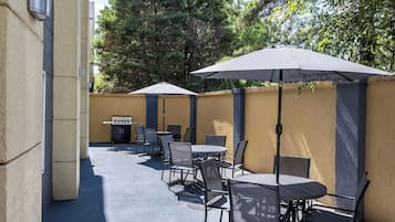Un patio al aire libre con mesas, sillas, una parrilla y sombrillas que dan sombra.