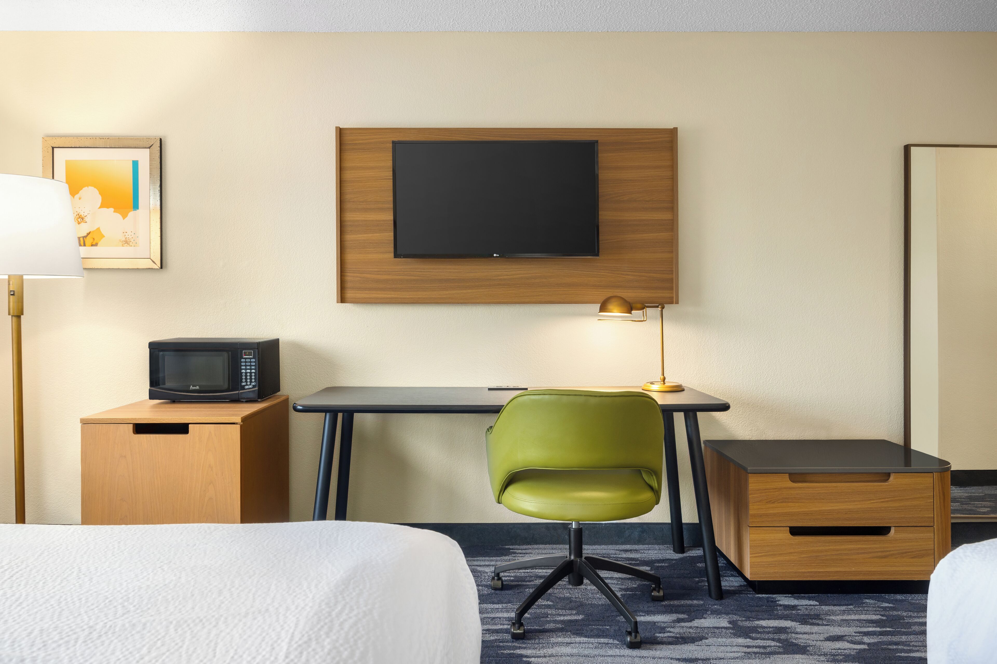A hotel room with a bed, a desk with a chair, a television, a microwave, and a lamp.