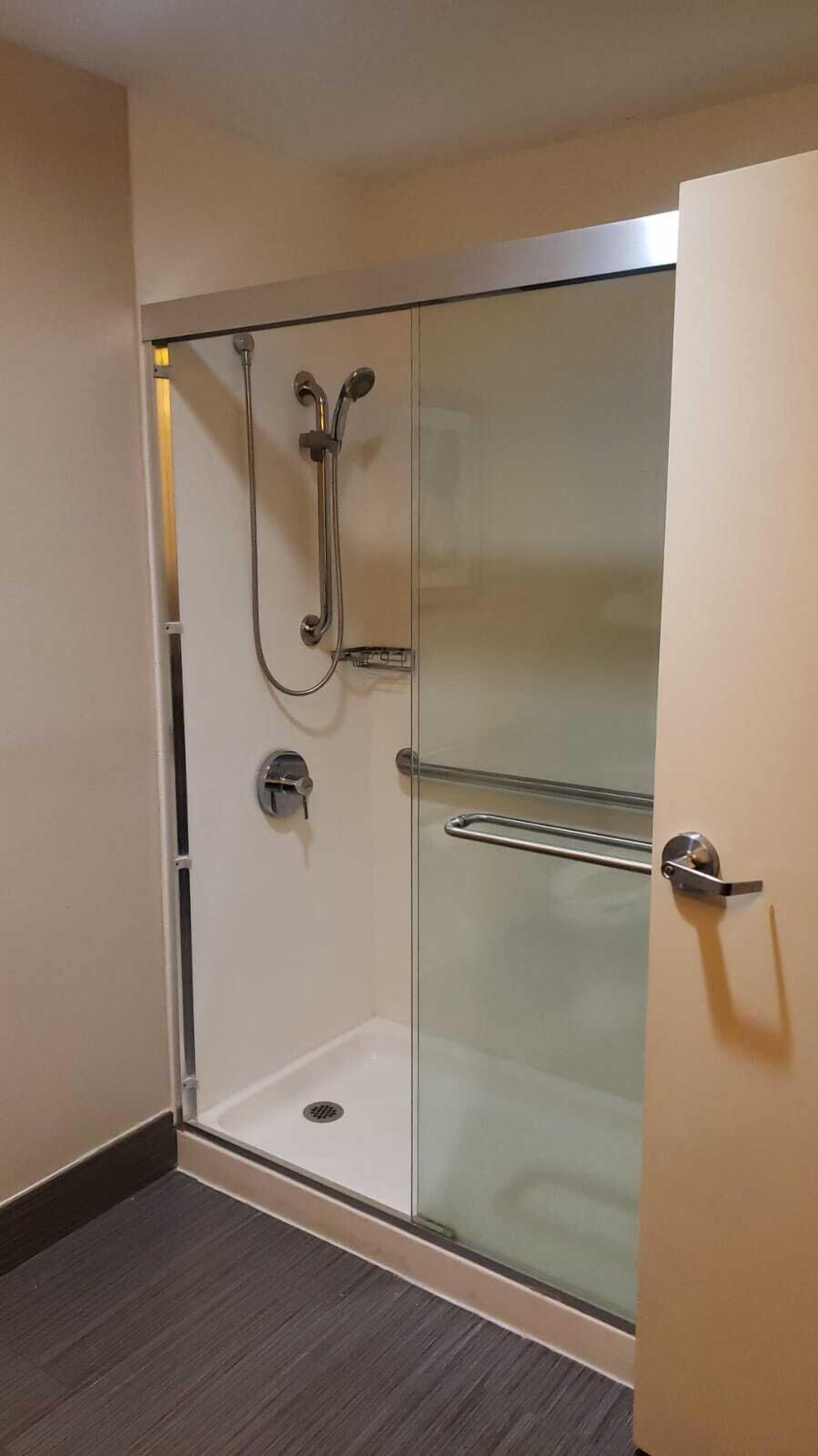Une cabine de douche fermée par des parois en verre, dotée d’un pommeau de douche à main et d’une porte en verre.