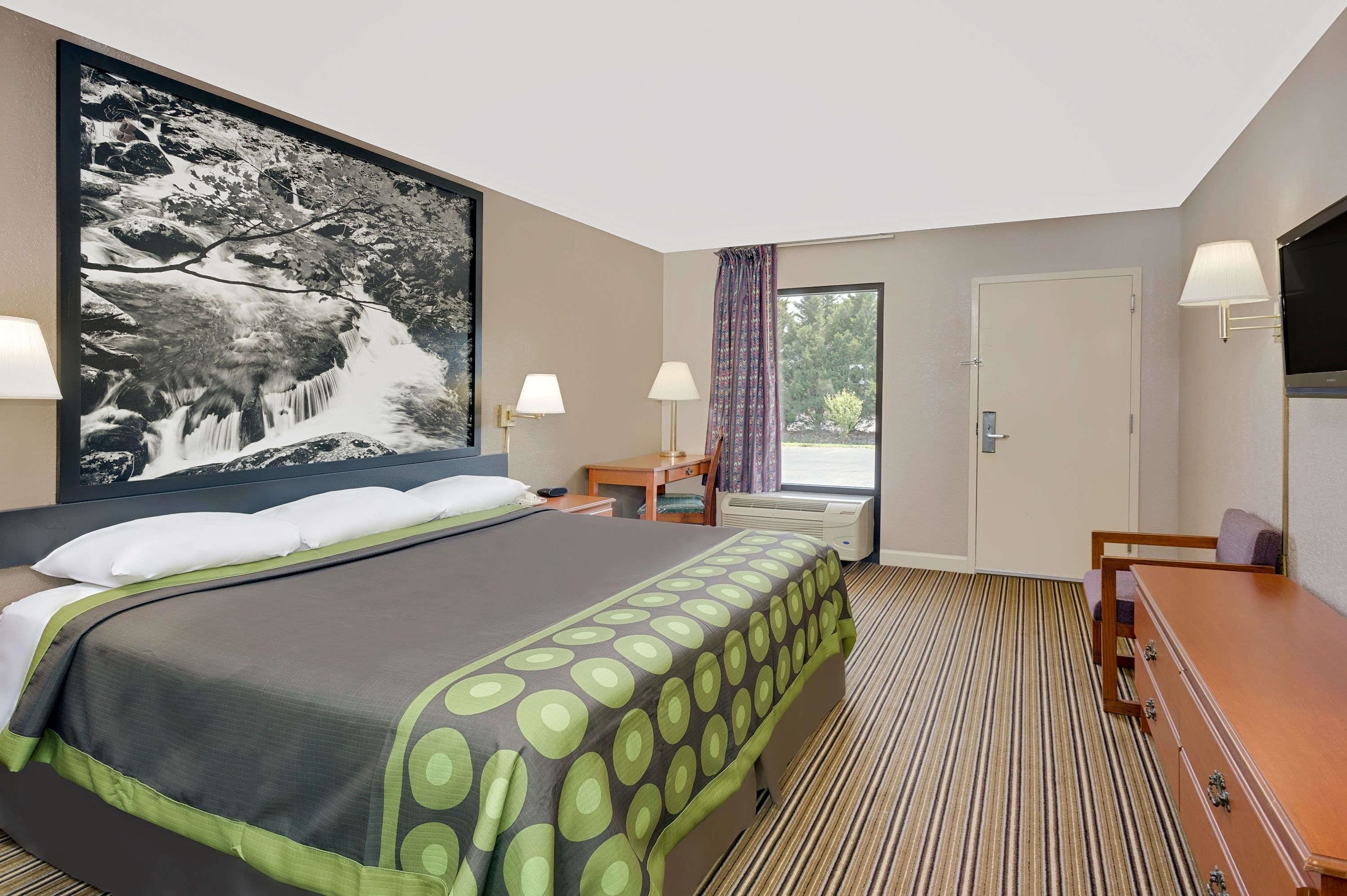 Une chambre d’hôtel avec un grand lit, deux tables de chevet, un bureau et une vue sur un balcon.