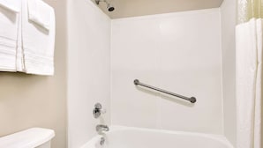 Une salle de bain avec une baignoire blanche, une douche et des toilettes. Un porte-serviettes fixé au mur porte deux serviettes.