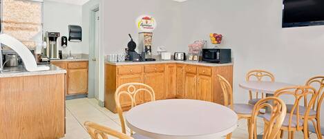 Una cocina moderna con armarios de madera, una barra desayunadora, una cafetera y un microondas. Hay mesas redondas y sillas para comer.