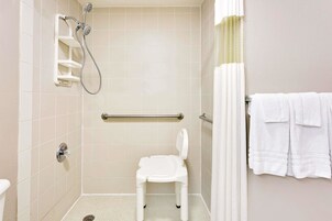 Un baño con inodoro blanco, ducha con barra de apoyo y toallero con toallas.
