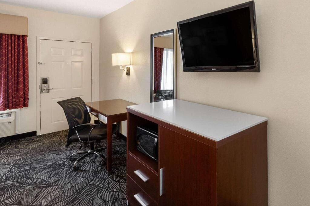 A hotel room with a desk, chair, television, and a wardrobe.