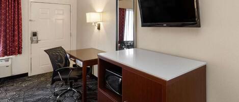 Een hotelkamer met een bureau, stoel, televisie en een kledingkast.