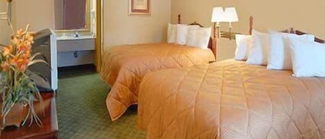 A hotel room with two beds, a desk, a lamp, and a framed picture on the wall.