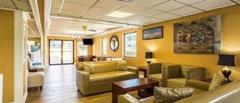 A hotel lobby with a wooden floor, leather sofas, a coffee table, and a clock on the wall.
