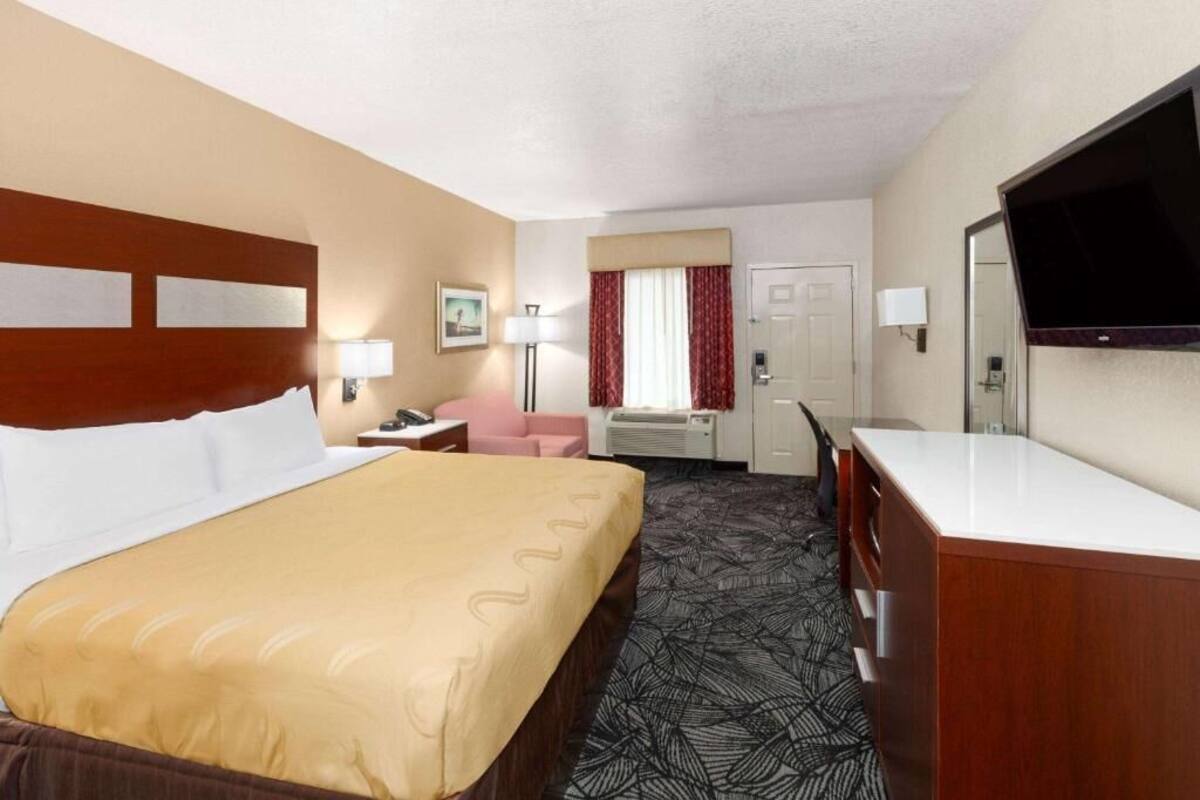A hotel room with a large bed, a desk, a chair, a television, and a window with curtains.