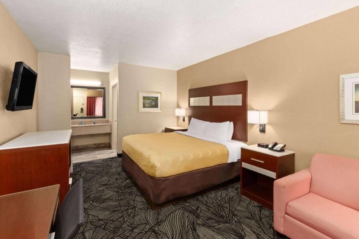 A hotel room with a bed, bedside table, lamp, and a television mounted on the wall.