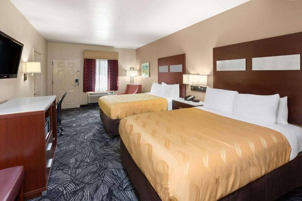 A hotel room with two beds, a desk, a chair, and a TV.
