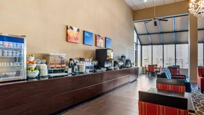 A modern hotel lobby with a long reception counter, a coffee machine, and seating area with red and black chairs. - Comfort Inn Pearl-Jackson (Pearl)