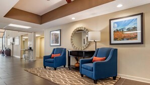 A spacious lobby with two blue armchairs, a patterned rug, a round mirror, framed artwork, and a desk with a lamp. - Comfort Inn Pearl-Jackson (Pearl)