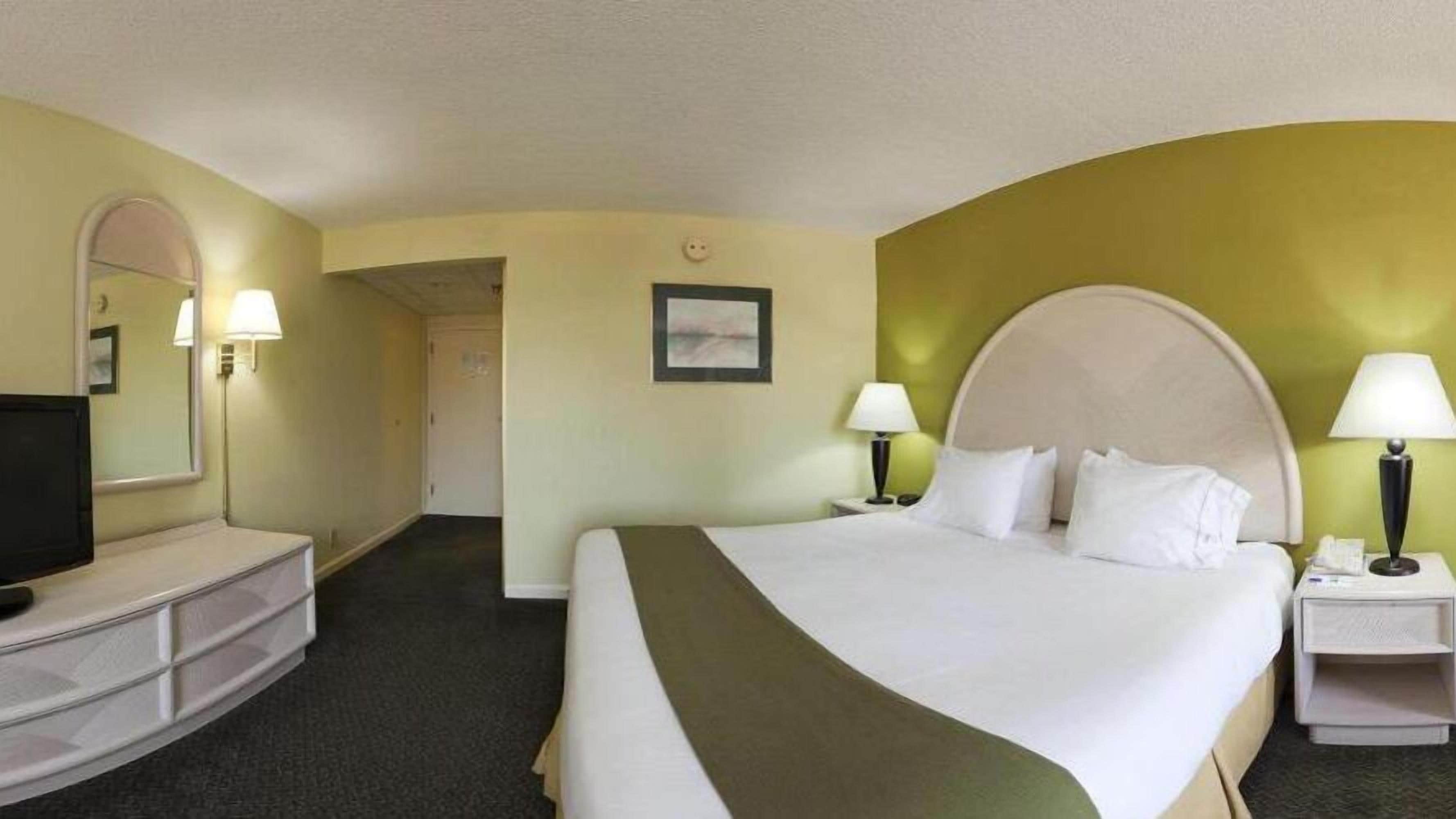 Quarto de hotel com uma cama grande, televisão, escrivaninha e uma cadeira.