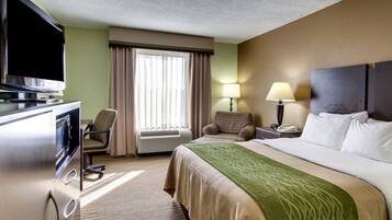 Habitación de hotel con cama, televisión, escritorio, silla, lámpara y ventana con cortinas.