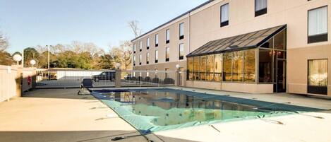 A modern building with a swimming pool, a covered patio, and a gated entrance.