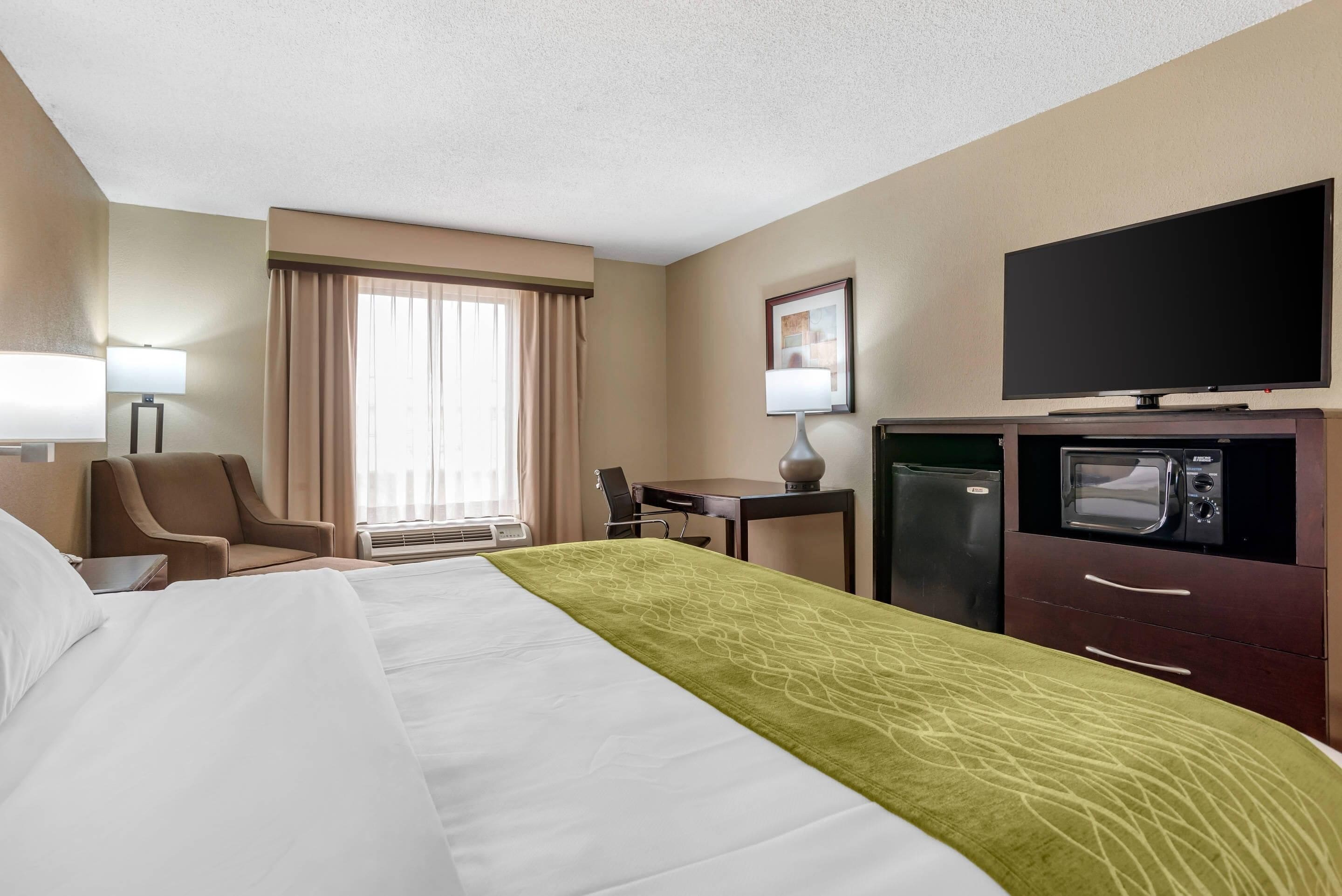 A hotel room with a bed, a desk, a television, a microwave, and a refrigerator.