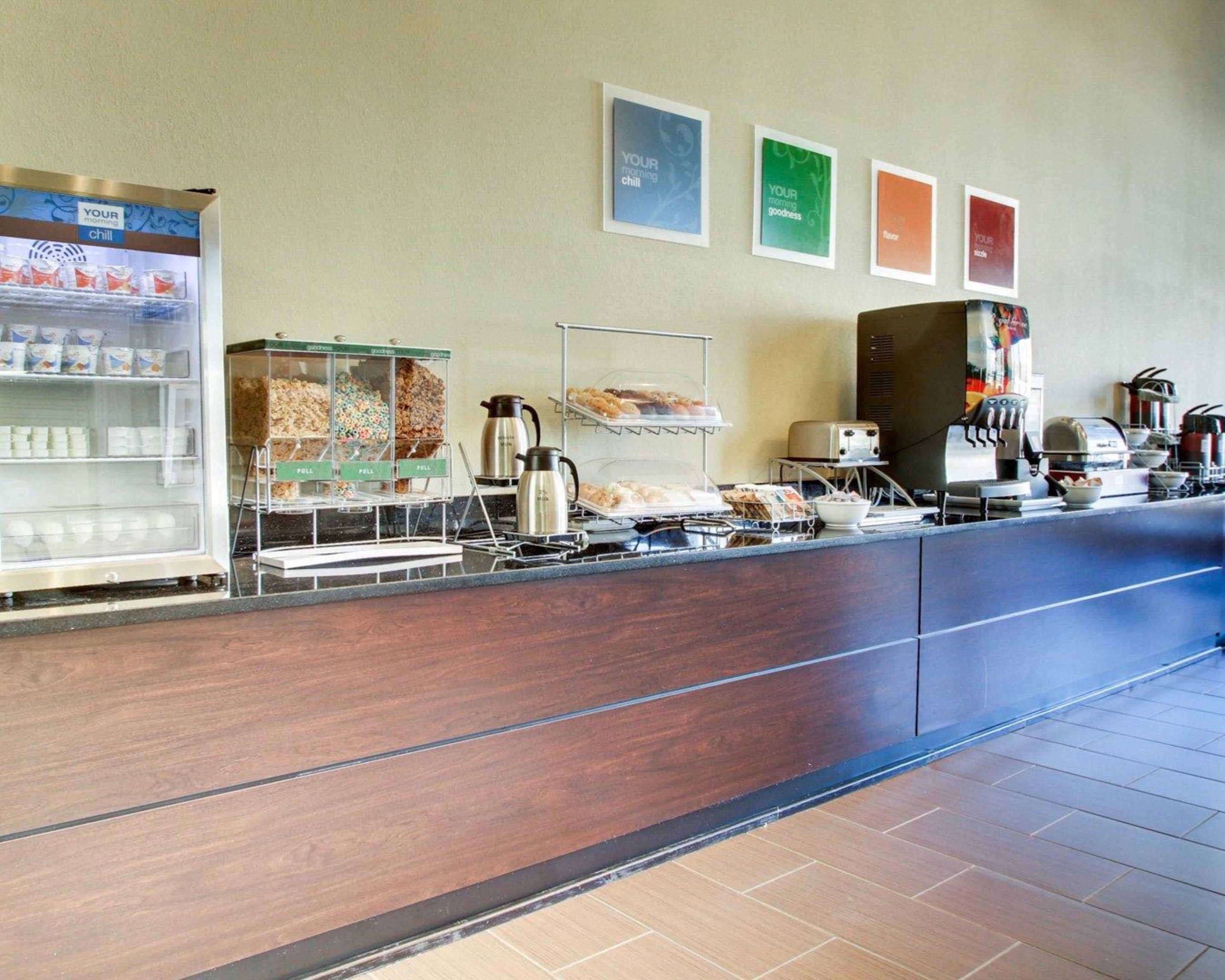 A buffet area with various food items, a coffee station, and a refrigerator with beverages.